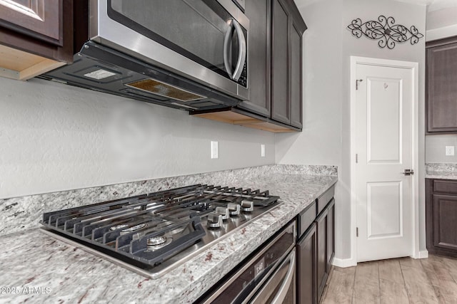 kitchen featuring appliances with stainless steel finishes, dark brown cabinets, and light stone countertops