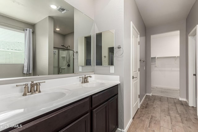 bathroom featuring a shower stall, wood finished floors, a spacious closet, double vanity, and baseboards