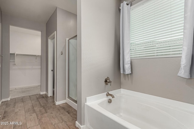 full bath featuring a shower stall, a spacious closet, a garden tub, wood finished floors, and baseboards