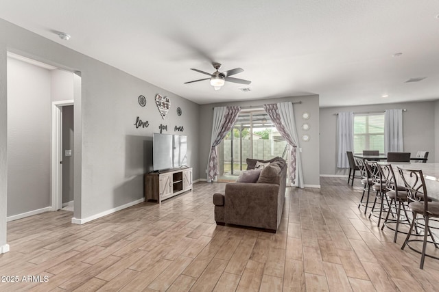 living area featuring light wood finished floors, a ceiling fan, and baseboards