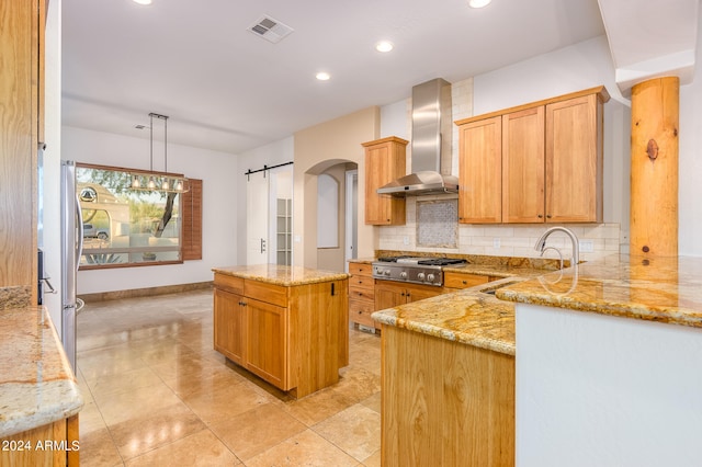 kitchen featuring hanging light fixtures, a barn door, wall chimney exhaust hood, stainless steel gas cooktop, and sink