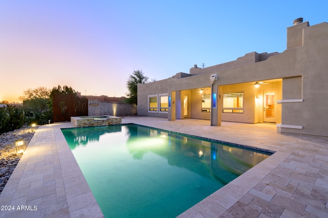 pool at dusk featuring a patio and an in ground hot tub