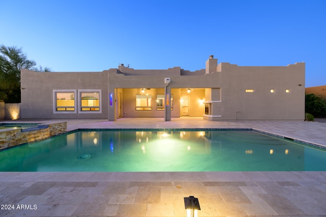 pool at dusk featuring a patio and an in ground hot tub