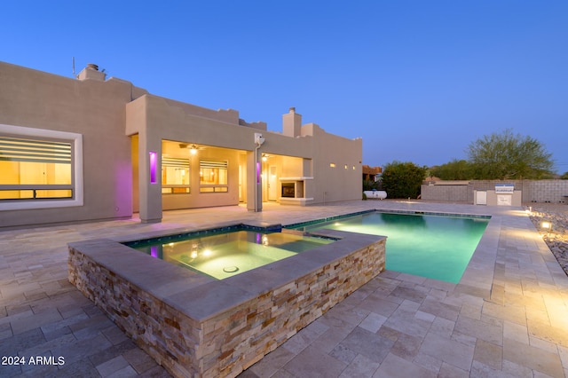 pool at dusk with an in ground hot tub and a patio area