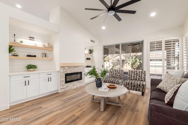 living room with ceiling fan, a fireplace, lofted ceiling, and light wood-type flooring