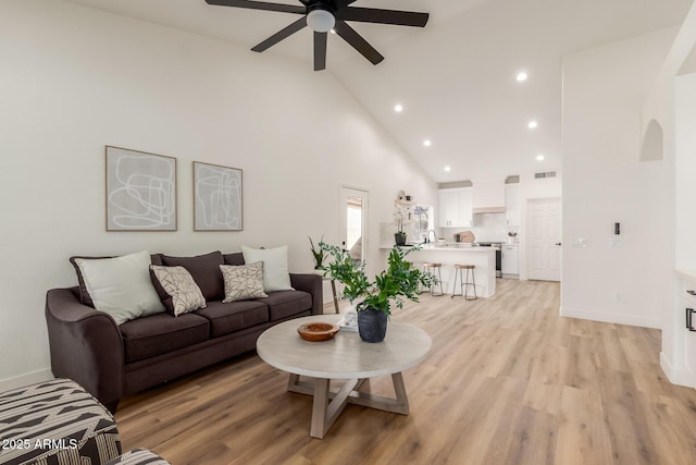 living room featuring ceiling fan, light wood-type flooring, sink, and high vaulted ceiling