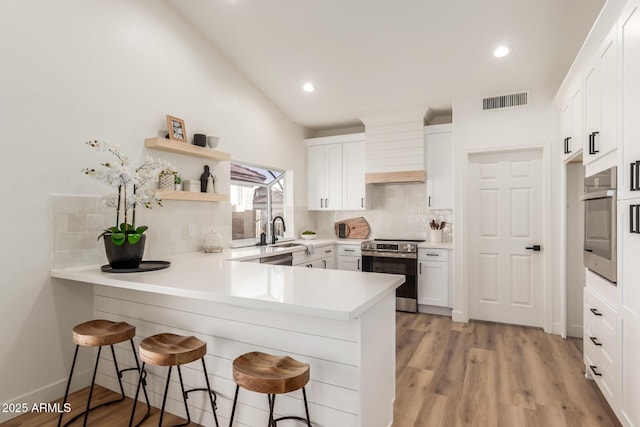 kitchen with a kitchen breakfast bar, white cabinetry, tasteful backsplash, and appliances with stainless steel finishes