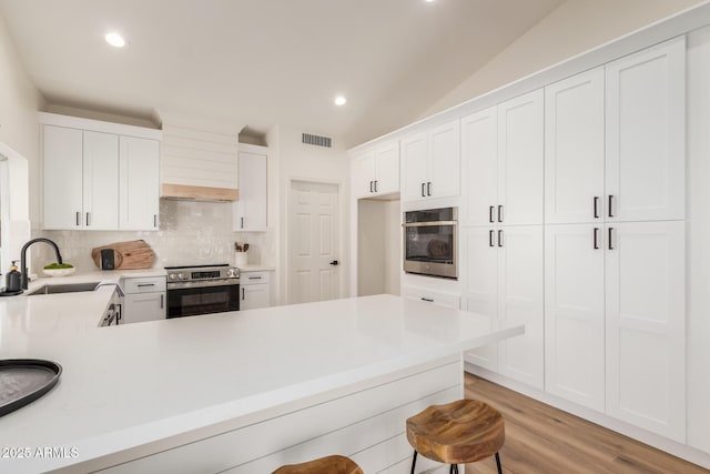 kitchen with sink, stainless steel appliances, lofted ceiling, decorative backsplash, and white cabinets