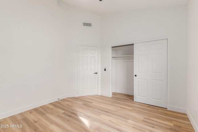 unfurnished bedroom with a closet, a high ceiling, and light hardwood / wood-style flooring