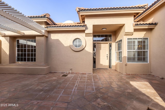 view of exterior entry featuring a patio area and a pergola