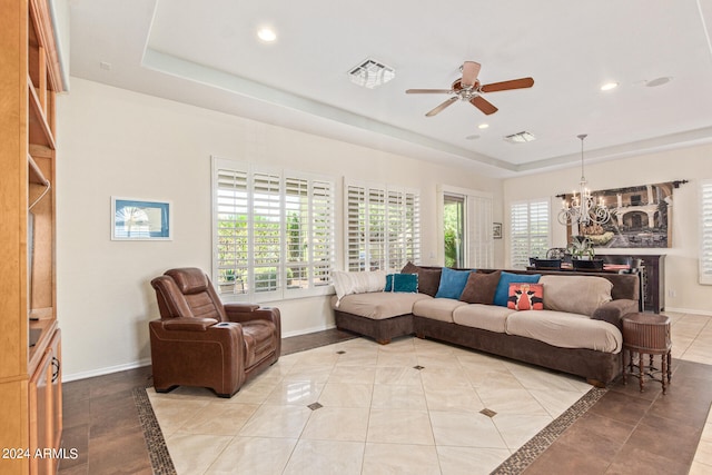 tiled living room with ceiling fan with notable chandelier and a tray ceiling