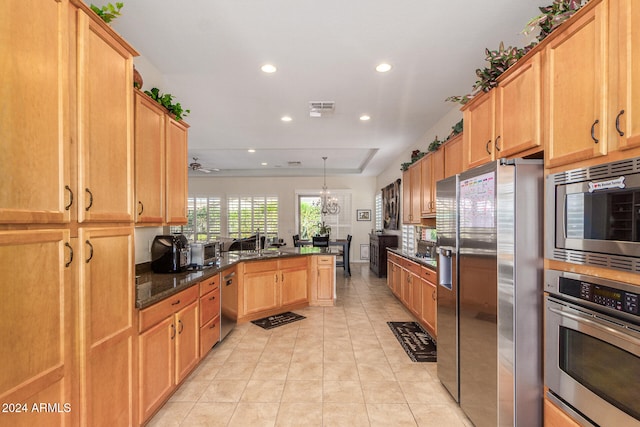 kitchen with stainless steel appliances, dark stone countertops, kitchen peninsula, hanging light fixtures, and a chandelier