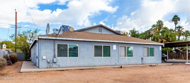 rear view of property featuring a shingled roof, fence, and stucco siding