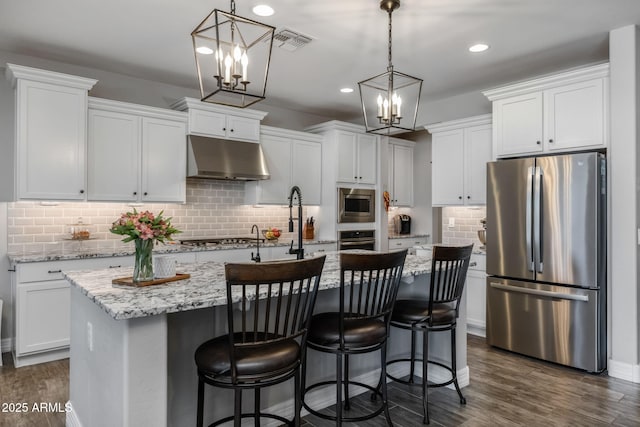 kitchen featuring white cabinets, stainless steel appliances, hanging light fixtures, and an island with sink