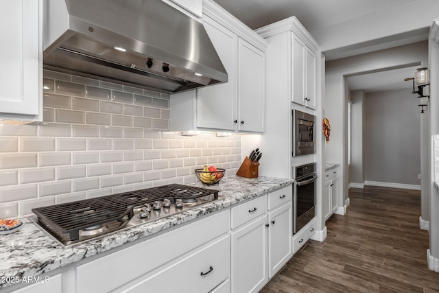 kitchen with white cabinets, light stone countertops, range hood, tasteful backsplash, and stainless steel appliances