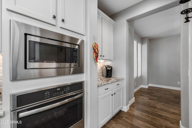 kitchen featuring appliances with stainless steel finishes, dark hardwood / wood-style flooring, tasteful backsplash, light stone counters, and white cabinetry