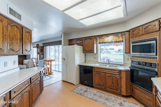 kitchen with sink, a textured ceiling, light hardwood / wood-style flooring, black appliances, and vaulted ceiling