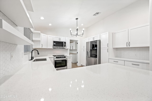 kitchen with appliances with stainless steel finishes, vaulted ceiling, sink, pendant lighting, and white cabinetry