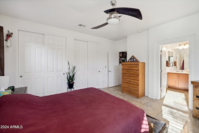 bedroom featuring visible vents, two closets, ensuite bathroom, a ceiling fan, and light tile patterned floors