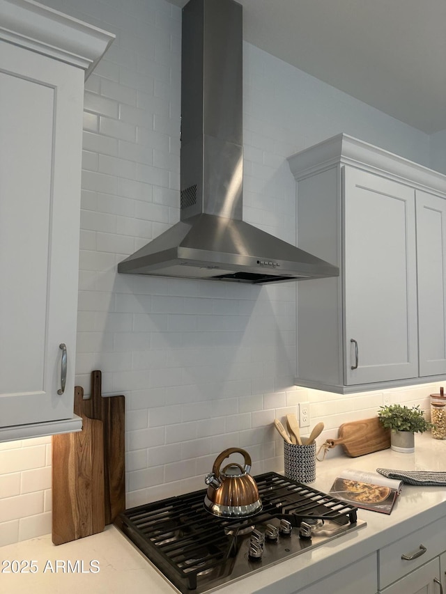 kitchen featuring stainless steel gas stovetop, white cabinetry, tasteful backsplash, and wall chimney exhaust hood