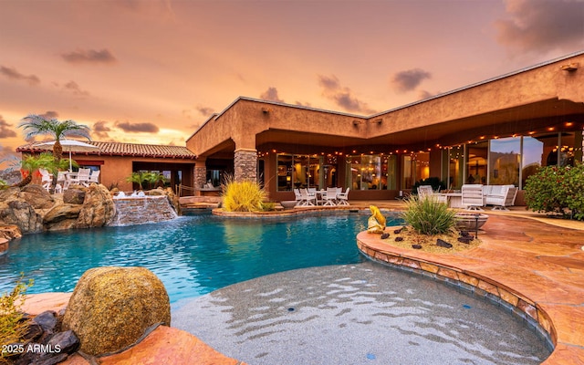 pool at dusk with a patio area and an outdoor pool