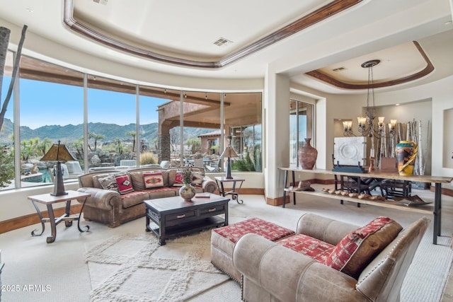 living area with a tray ceiling, visible vents, an inviting chandelier, a mountain view, and baseboards