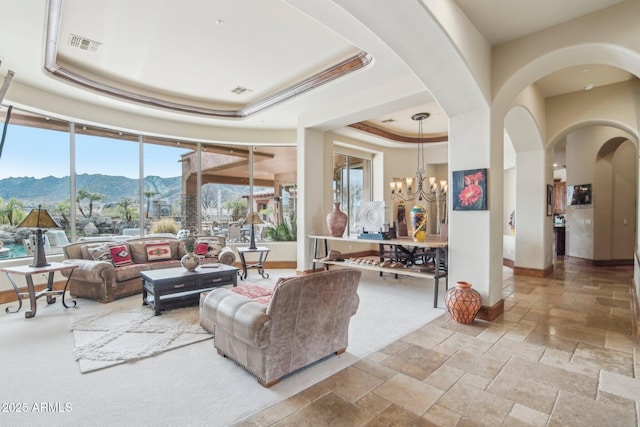 living room featuring a tray ceiling, stone tile flooring, a mountain view, and a notable chandelier