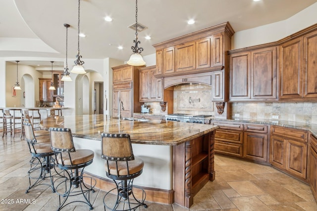 kitchen featuring arched walkways, visible vents, backsplash, brown cabinets, and a kitchen bar