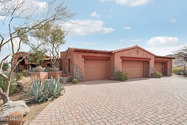 mediterranean / spanish house with decorative driveway, an attached garage, a tile roof, and stucco siding