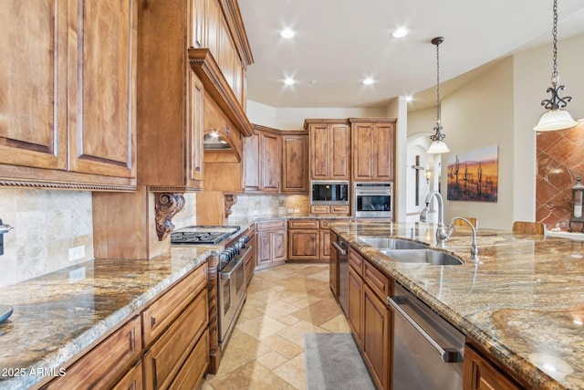 kitchen with a sink, appliances with stainless steel finishes, backsplash, brown cabinetry, and decorative light fixtures