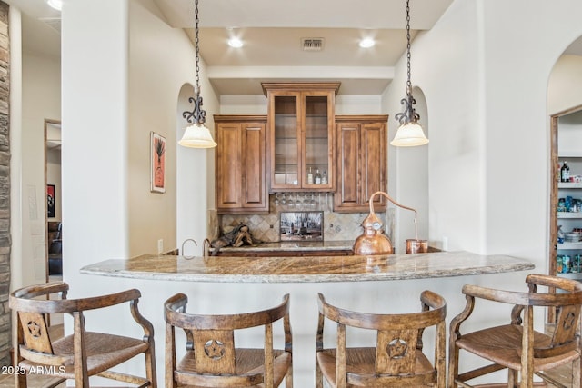 kitchen with brown cabinetry, a breakfast bar, visible vents, and decorative backsplash