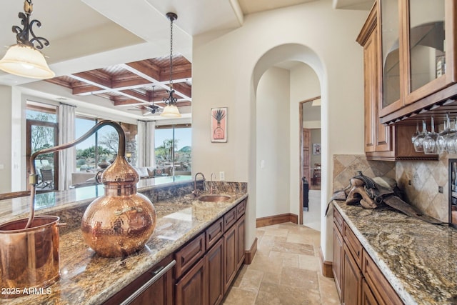 kitchen with arched walkways, stone tile floors, coffered ceiling, a sink, and decorative backsplash