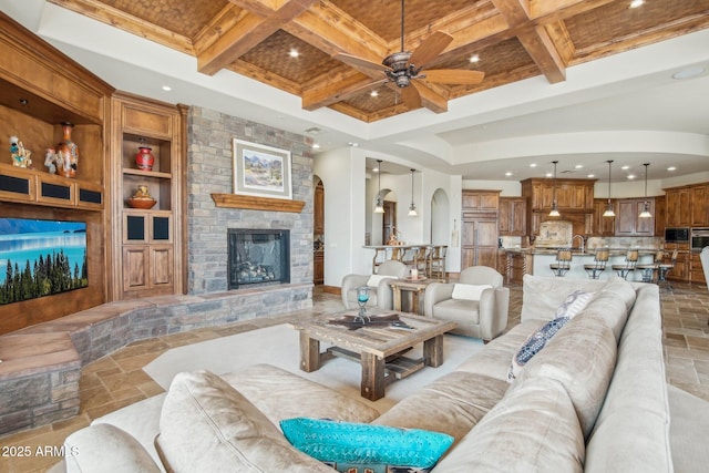 living area with built in shelves, stone tile floors, coffered ceiling, a fireplace, and beam ceiling