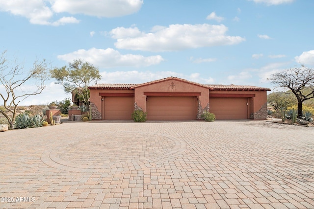 mediterranean / spanish-style home featuring a garage, a tile roof, decorative driveway, and stucco siding