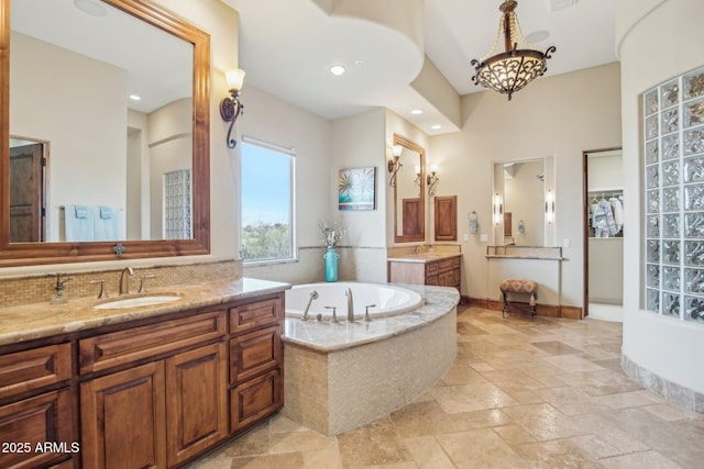 bathroom with a garden tub, stone tile floors, two vanities, a sink, and an inviting chandelier