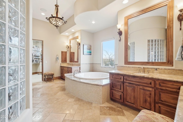 bathroom with a sink, a garden tub, an inviting chandelier, stone tile flooring, and two vanities