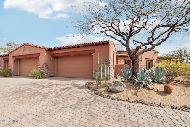 mediterranean / spanish-style house featuring a garage, a tiled roof, decorative driveway, and stucco siding