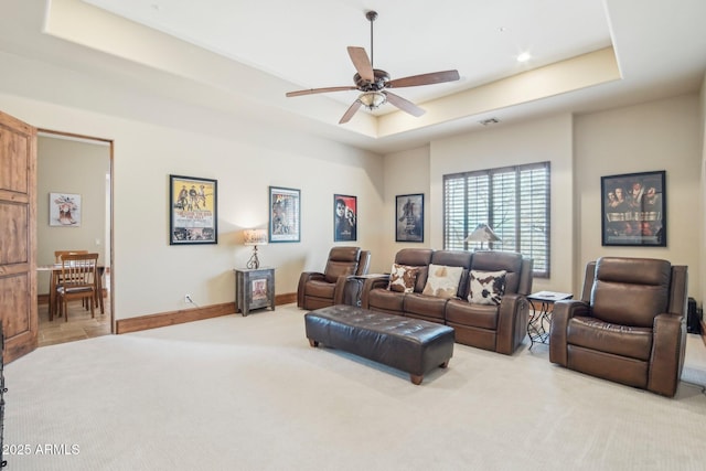 living room featuring a tray ceiling, light colored carpet, visible vents, a ceiling fan, and baseboards