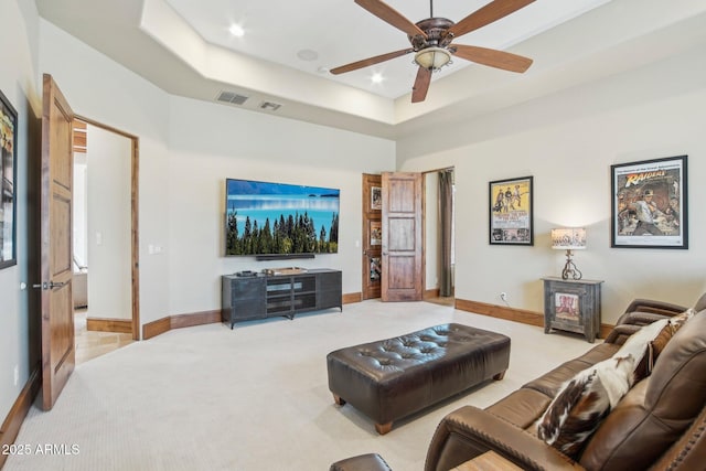 living room featuring baseboards, a tray ceiling, ceiling fan, and light colored carpet