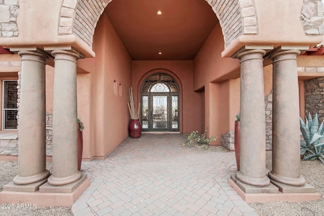 entrance to property with stone siding, french doors, and stucco siding