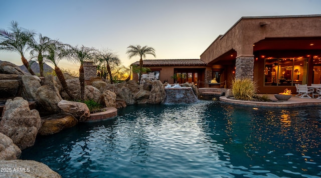 pool at dusk with a patio area, an outdoor pool, a fire pit, and a jacuzzi