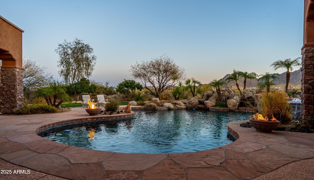 pool at dusk with a fire pit, a patio, and an outdoor pool