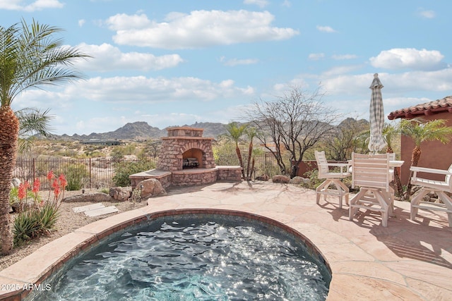 view of swimming pool featuring an outdoor stone fireplace, a patio, a mountain view, fence, and a jacuzzi