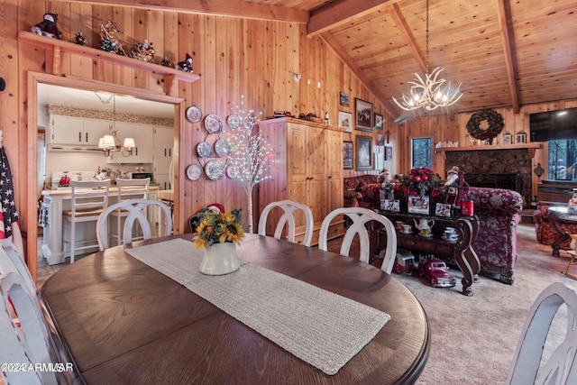 carpeted dining room featuring wood walls, a stone fireplace, lofted ceiling with beams, wooden ceiling, and an inviting chandelier