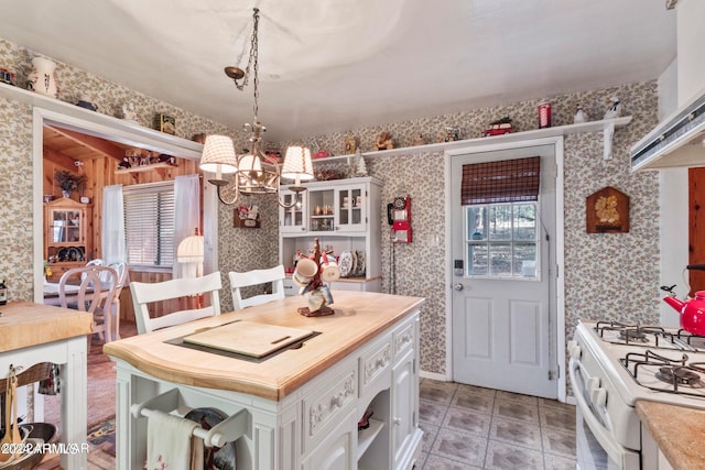 kitchen with decorative light fixtures, white cabinets, tile floors, a chandelier, and wall chimney range hood