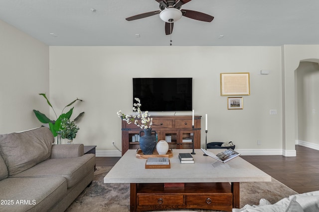 living room featuring arched walkways, ceiling fan, dark wood-style flooring, and baseboards