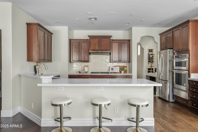 kitchen featuring stainless steel appliances, visible vents, decorative backsplash, a peninsula, and under cabinet range hood