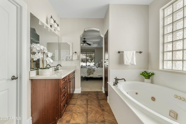 ensuite bathroom with double vanity, a ceiling fan, connected bathroom, a sink, and a tub with jets