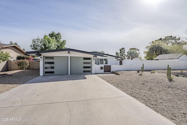 mid-century inspired home with a garage, concrete driveway, and fence