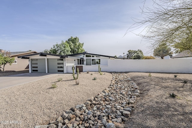 mid-century modern home featuring a garage, driveway, and fence